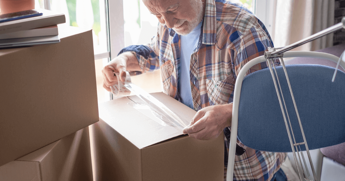 Senior man downsizing his home and packing up his items in a box.