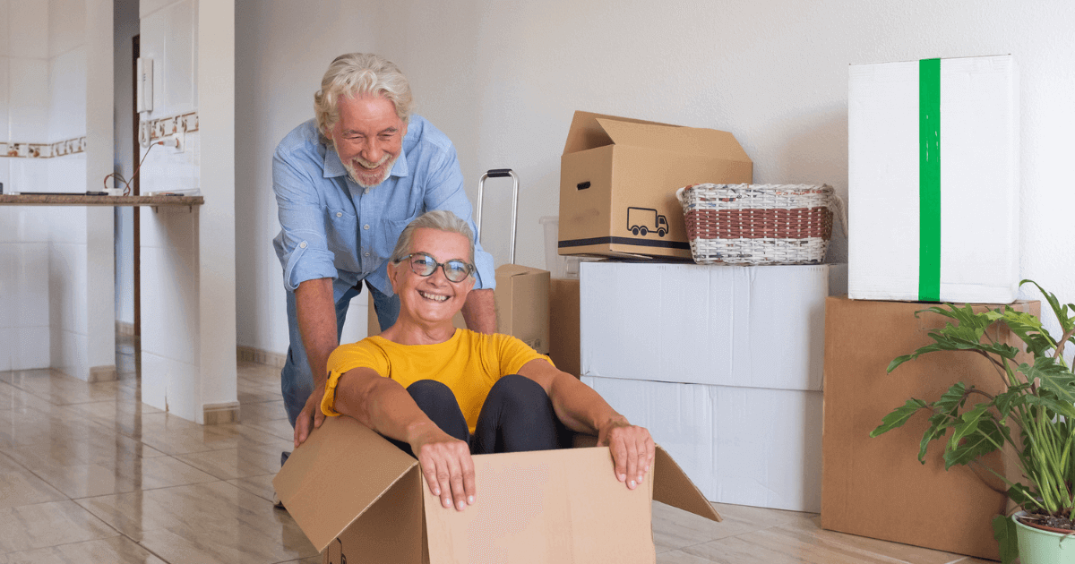 Senior man pushing his senior husband in a moving box smiling.