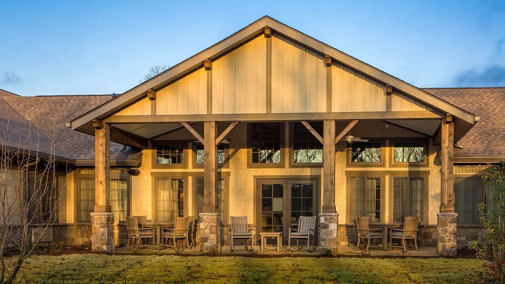 Exterior view of a Thrive Senior Living house with a large covered patio, wooden beams, stone pillars, glass doors, and inviting outdoor seating.