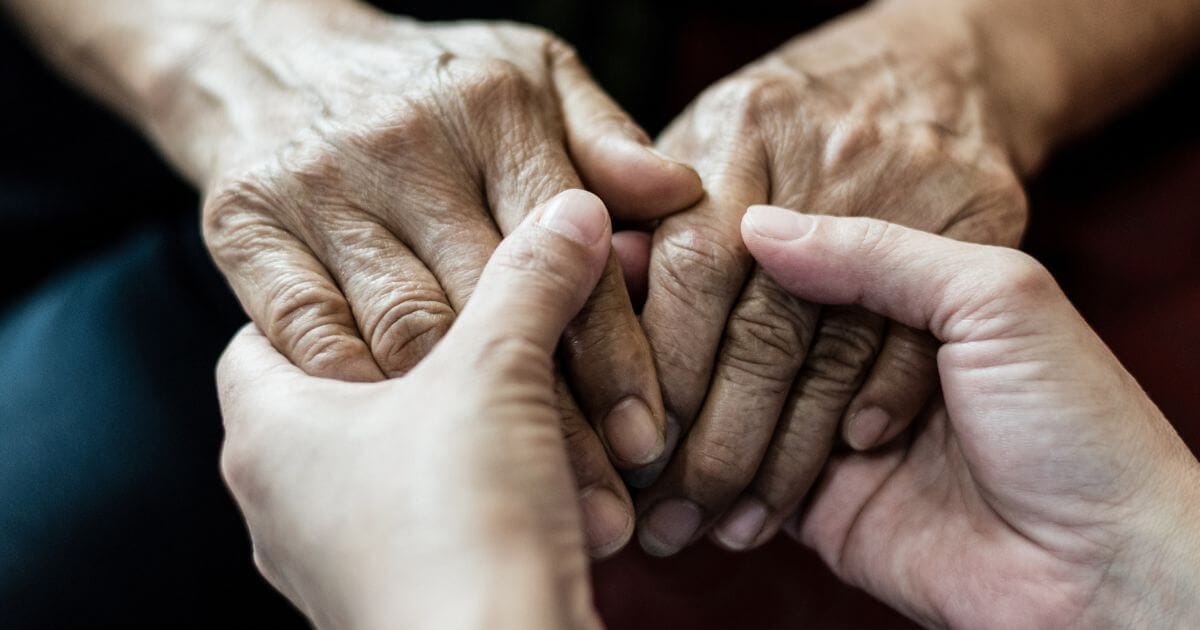 Close-up of two younger hands gently holding the hands of an older person, suggesting support and care at Thrive Senior Living.