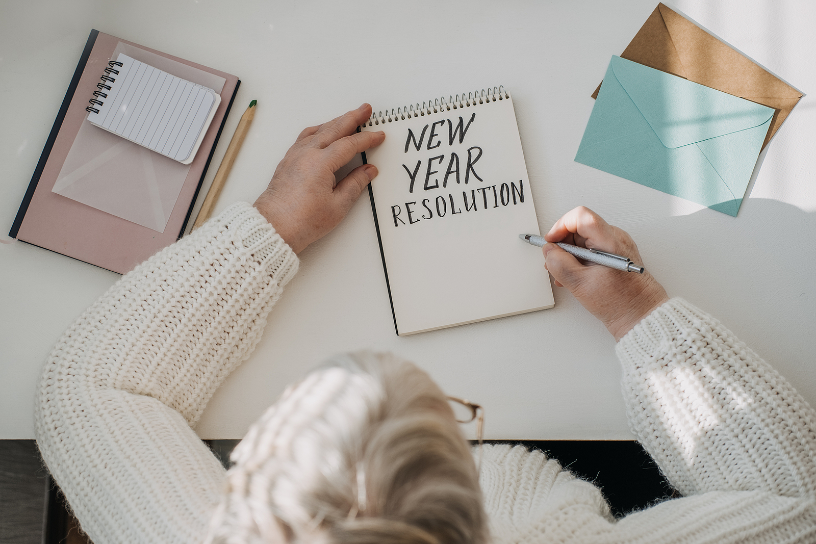 Senior woman sitting at desk writing down New Year’s resolutions for seniors