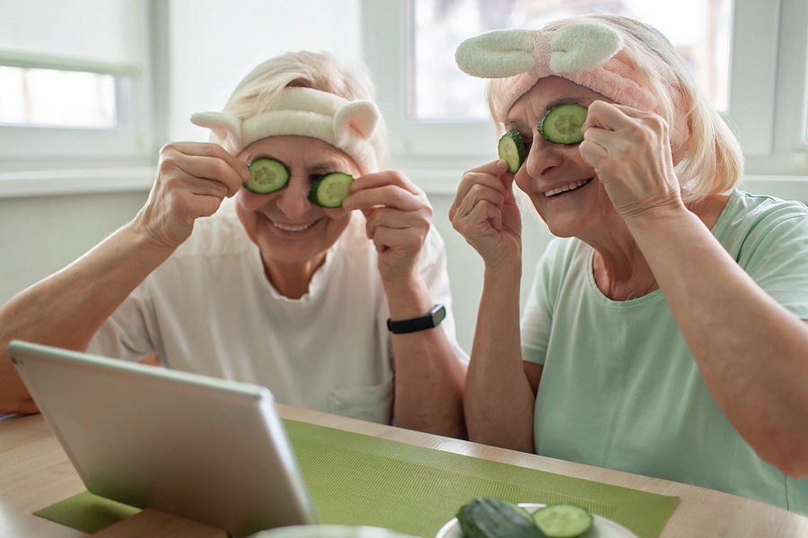 Two senior women focus on senior wellness while relaxing with face masks and using technology.